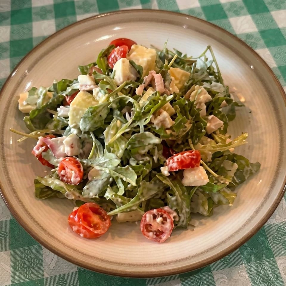 A fresh arugula salad with cherry tomatoes, cheese cubes, and ham, dressed in a creamy sauce.